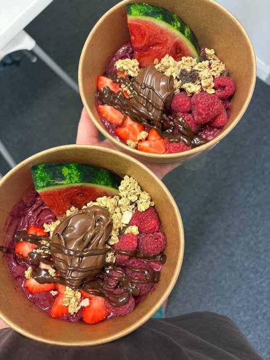 Two açaí bowls topped with strawberries, raspberries, watermelon, granola and chocolate.