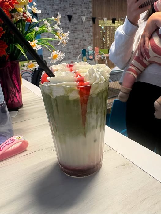 A tall layered milkshake topped with whipped cream and strawberry sauce.